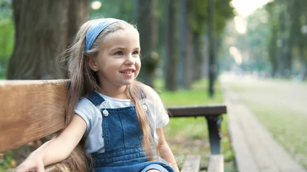 Petite fille heureuse assise sur un banc souriant joyeusement dans un parc d'été — Photo