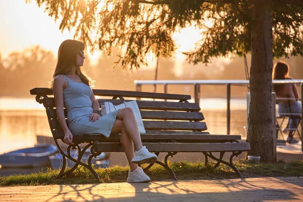Einsame Frau, die an einem warmen Sommerabend allein auf der Bank am Seeufer sitzt. Einsamkeit und Entspannung in der Natur — Stockfoto