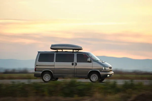 Passenger van with roof rack driving fast on intercity road at sunset. Highway traffic in evening — Stock Photo, Image