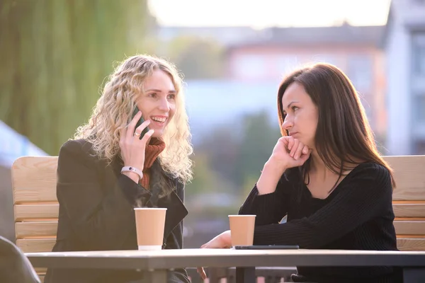 Unhappy young woman waiting angrily while her friend is talking happily on sellphone with someone else and ignoring her. Friendship problems concept — Stock Photo, Image