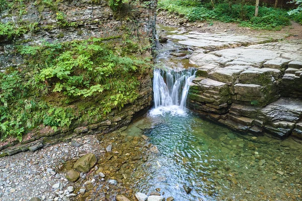 Vodopád na horské řece s bílou pěnovou vodou padající ze skalnatého útvaru v letním lese — Stock fotografie