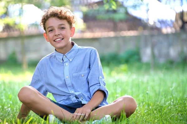 Young happy child boy relaxing on green grass in summer park. Positive kid enjoying summertime outdoors. Child wellbeing concept — Stock Photo, Image