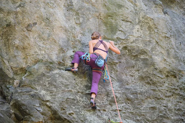 若い女性岩の山の急な壁を登る。登山家は困難な道を克服します。極端なスポーツの概念に従事 — ストック写真