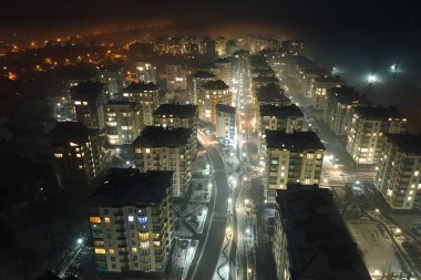 Yüksek katlı apartman binalarının ve şehrin yerleşim alanındaki aydınlık sokakların havadan görüntüsü. Karanlık şehir manzarası