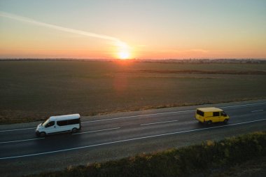 Gün batımında hızlı giden arabalarla şehirlerarası yol manzarası. Akşamları otoban trafiğinin insansız hava aracı görüntüsü