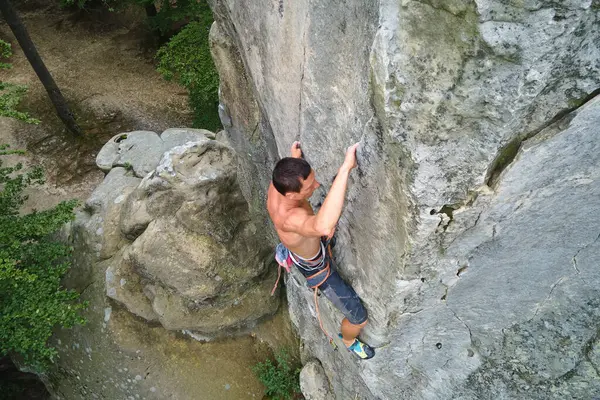 Determined climber clambering up steep wall of rocky mountain. Sportsman overcoming difficult route. Engaging in extreme sports and rock climbing hobby concept — Stock Photo, Image