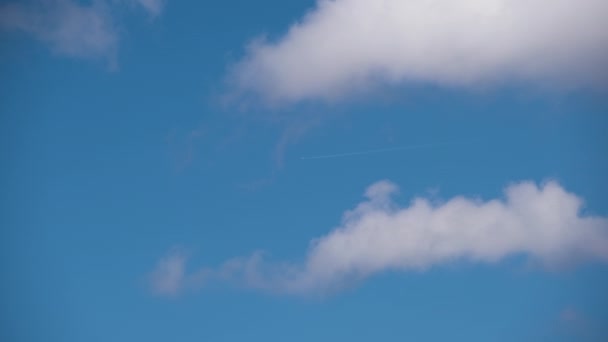 Pesawat jet penumpang yang jauh terbang di ketinggian tinggi di langit biru dengan awan putih meninggalkan jejak asap kontrail di belakang. Konsep perjalanan udara — Stok Video