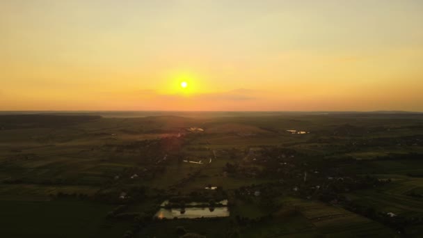 Aerial landscape view of green cultivated agricultural fields with growing crops and distant village houses on bright summer evening — Stockvideo