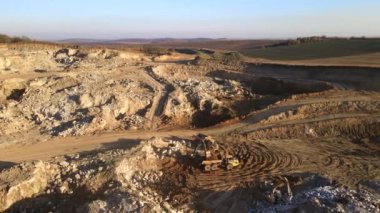 Kazı makineleri ve çöp kamyonlarıyla inşaat endüstrisi için kumtaşı malzemelerinden oluşan açık maden manzarası. Madencilik ve kullanışlı mineral üretiminde ağır ekipman