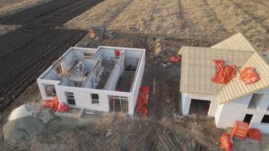 Havalandırılmış hafif beton duvarları ve yapım aşamasındaki ahşap çatı iskeleti olan bitmemiş özel evin havadan görüntüsü.