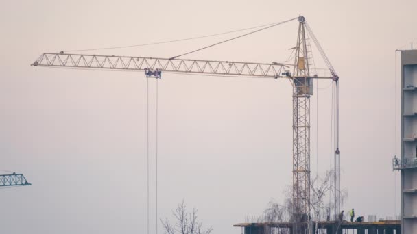 Silueta oscura de la grúa torre y pequeñas siluetas de los trabajadores en el sitio de construcción de apartamentos residenciales de alta. Desarrollo inmobiliario — Vídeos de Stock