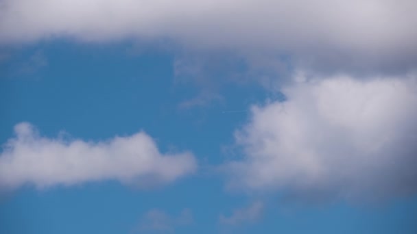 Avião de passageiros distantes voando em alta altitude no céu azul com nuvens brancas deixando vestígios de fumaça de contrail para trás. Conceito de viagem aérea — Vídeo de Stock