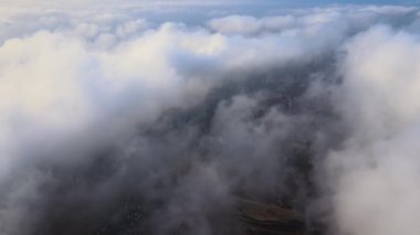 Fırtınadan önce, şişkin kümülüs bulutlarıyla kaplı uzak şehrin yüksek irtifasından gelen hava manzarası. Bulutlu havada uçak manzarası