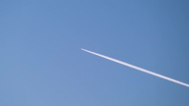 Mesafeli yolcu jet uçağı açık mavi gökyüzünde yüksek irtifada uçarken ardında beyaz duman izi bırakıyor. Hava taşımacılığı kavramı