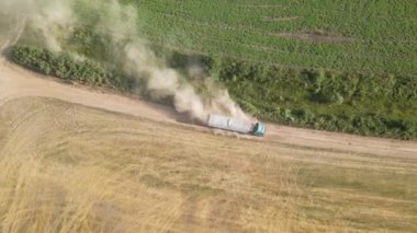 Tarım buğday tarlaları arasında toprak yolda giden kargo kamyonunun hava görüntüsü çok toz yapıyor. Hasat mevsiminde hasatçıların topladığı tahıl naklinden sonra.
