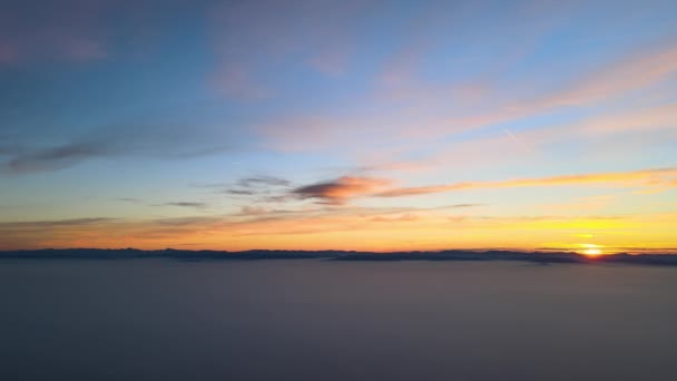 Vista aérea de colorido atardecer sobre nubes de niebla blanca densa cubierta con siluetas oscuras distantes de colinas de montaña en el horizonte — Vídeo de stock