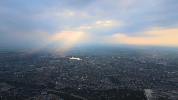 遠くの都市の高高度からの空中ビューは、日没時に暴風雨の前に飛んでパフィー積雲で覆われています。曇天下における景観の航空機の視点 — ストック動画