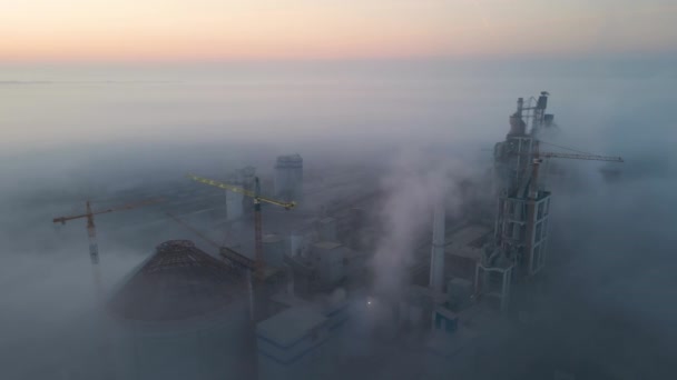 Вид с воздуха на цементный завод с высокой конструкцией бетонного завода и башенный кран на производственной площадке в туманное утро. Концепция производства и мировой промышленности — стоковое видео
