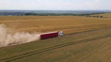 Tarımsal buğday tarlaları arasında toprak yolda giden kamyon görüntüsü. Hasat mevsiminde hasatçıların topladığı tahıl naklinden sonra.