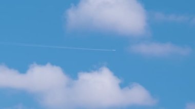 Uzaktaki yolcu uçağı mavi gökyüzünde yüksek irtifada uçarken beyaz bulutlar ardında iz bırakıyor. Hava yolculuğu konsepti
