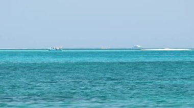 Mavi deniz suyunun dalgalı yüzeyi ve sakin dalgalar üzerinde yüzen uzak gemileri olan deniz burnu.