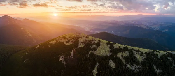 Luftaufnahme einer atemberaubenden Landschaft mit nebelverhangenem, dunklem Berggipfel, der bei Sonnenaufgang im Herbst mit Kiefern bedeckt ist. Schöne wilde Wälder mit leuchtenden Lichtstrahlen im Morgengrauen — Stockfoto