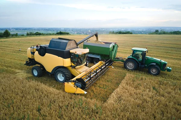 Aerial view of combine harvester unloading grain in cargo trailer working during harvesting season on large ripe wheat field. Agriculture and transportation of raw farm products concept — Stockfoto