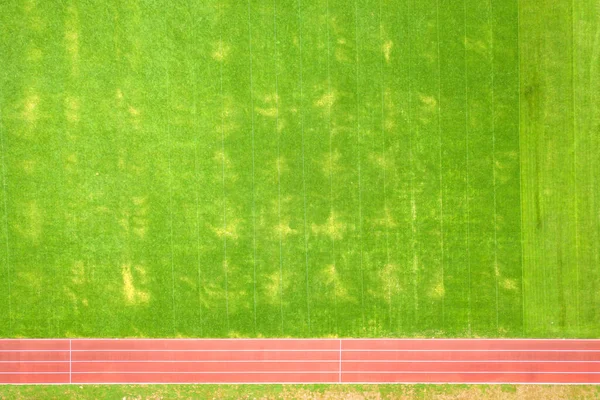 Vista aérea da superfície da grama verde recém-cortada no campo de estádio de futebol com pistas de corrida vermelhas no verão — Fotografia de Stock
