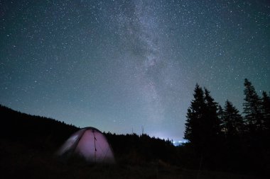 Parlak turist çadırı gece gökyüzünün altındaki karanlık dağlarda parlayan yıldızlarla parlıyordu. Etkin yaşam tarzı kavramı
