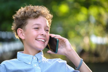 Yazlık parkta cep telefonuyla konuşan mutlu genç çocuk.