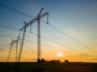 Gün batımında elektrik hatları olan yüksek voltaj kuleleri.