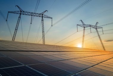 Elektrik hatları olan yüksek voltaj kuleleri günbatımında güneş fotovoltaik panellerinden enerji aktarıyor. Sürdürülebilir elektrik üretimi