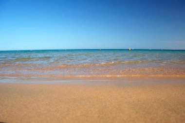 Mavi deniz suyunun yüzeyi ve küçük dalgalı dalgaların sarı kumsala çarptığı deniz burnu. Seyahat ve tatil kavramı