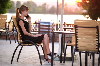 Genç bir kadın sıcak bir yaz akşamında sokak kafeteryasında cep telefonuyla konuşuyor. İletişim ve mobil bağlantı kavramı