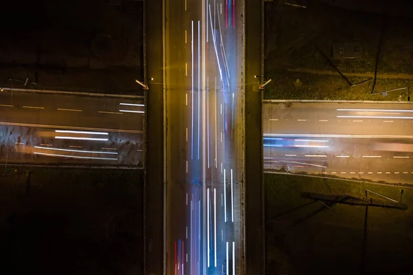 Vista aerea dell'incrocio stradale con traffico pesante in rapido movimento di notte. Vista dall'alto del trasporto urbano. Ora di punta con movimento sfocato auto luci sentiero — Foto Stock