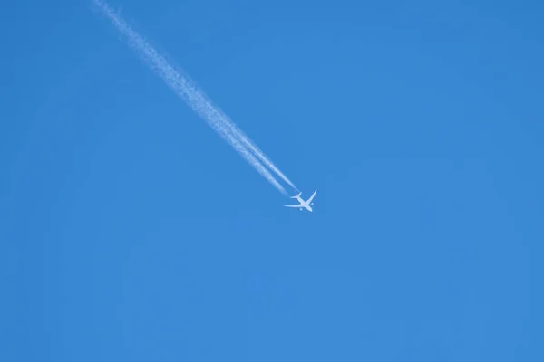 Avión a reacción de pasajeros a distancia volando a gran altitud en el cielo azul claro dejando rastro de humo blanco de la estela detrás. Concepto de transporte aéreo — Foto de Stock