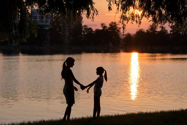 Happy mom and daughter girl relaxing holding hands enjoying time together in summer park at sunset. Family love and relationship concept — Stock Photo, Image
