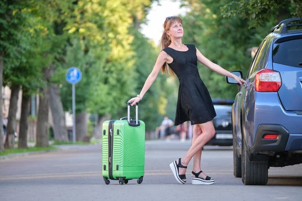 Glückliche junge Frau mit Koffertasche, die während einer Autofahrt neben ihrem Auto steht. Reise- und Urlaubskonzept — Stockfoto
