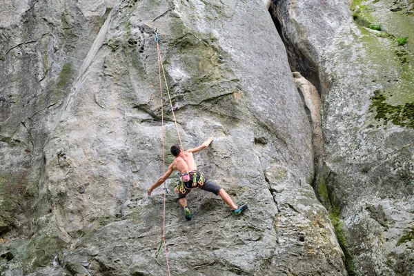 Forte alpinista do sexo masculino escalando parede íngreme de montanha rochosa. Esportista superando rota difícil. Envolvendo-se em conceito de passatempo esportivo extremo — Fotografia de Stock