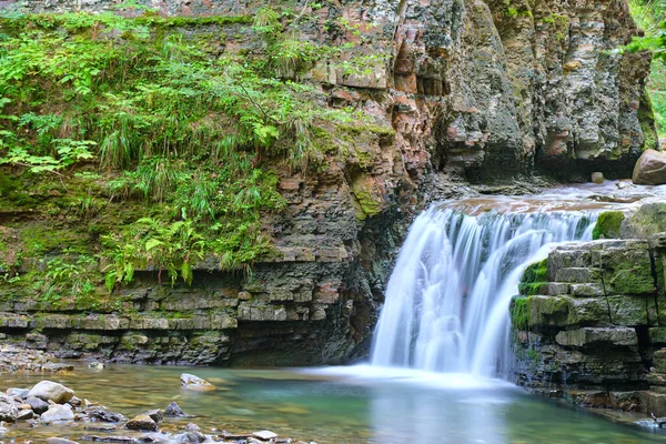 Vodopád na horské řece s bílou pěnovou vodou padající ze skalnatého útvaru v letním lese — Stock fotografie