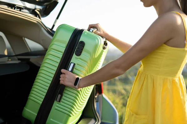 Junge Autofahrerin holt grünen Koffer aus dem Kofferraum Reise- und Urlaubskonzept — Stockfoto