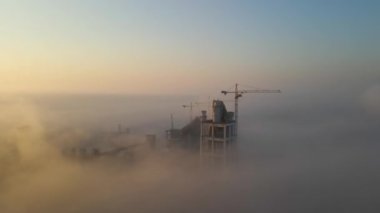 Yüksek beton yapılı çimento fabrikası ve sisli bir sabahta endüstriyel üretim alanında kule vinci. Üretim ve küresel sanayi kavramı