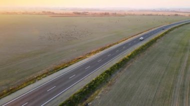 Gün batımında hızlı giden arabalarla şehirlerarası yol manzarası. Akşamları otoban trafiğinin insansız hava aracı görüntüsü