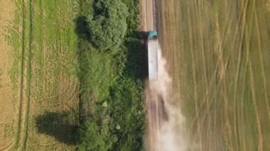 Tarımsal buğday tarlaları arasında toprak yolda giden kamyon görüntüsü. Hasat mevsiminde hasatçıların topladığı tahıl naklinden sonra.