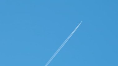 Mesafeli yolcu jet uçağı açık mavi gökyüzünde yüksek irtifada uçarken ardında beyaz duman izi bırakıyor. Hava taşımacılığı kavramı