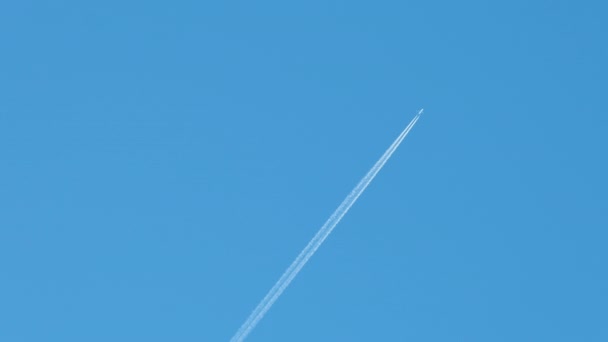 Avião de passageiros distantes voando em alta altitude no céu azul claro deixando vestígios de fumaça branca de contrail para trás. Conceito de transporte aéreo — Vídeo de Stock