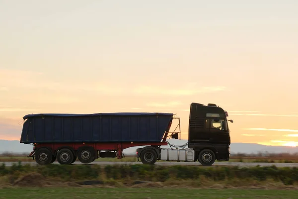 Semi-caminhão com reboque de carga derrubada transportando areia de pedreira dirigindo em mercadorias de transporte rodoviário à noite. Conceito de transporte e logística de entrega — Fotografia de Stock