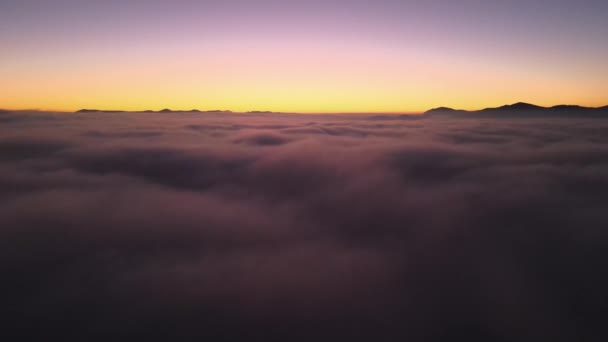 Luchtfoto van kleurrijke zonsopgang boven witte dichte mist met verre donkere silhouetten van berghellingen aan de horizon — Stockvideo