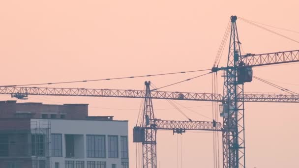 Silhouette sombre de grues à tour dans les immeubles résidentiels élevés chantier de construction au coucher du soleil. Développement immobilier. — Video