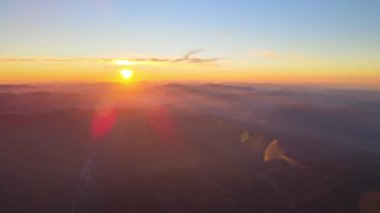 Gün batımında gün batımında parlak güneş ışınlarıyla karanlık dağ tepelerinin havadan görünüşü. Akşamları sisli tepeler ve sisli vadiler